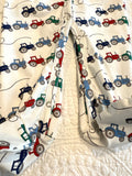 Bobbie's Shoppe white footed pajamas with all-over tractor print in red, blue, and green. Zipper closure.